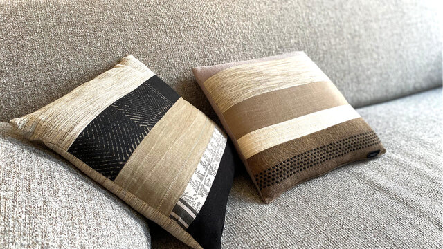 Nahaufnahme Designer-Sofa mit Dekokissen in gestreiften und strukturierten Mustern, nat&uuml;rliche Grau- und Beiget&ouml;ne mit verschiedenen Webstrukturen auf Salz-und-Pfeffer-Polster im m&ouml;blierten Apartment Bamberg