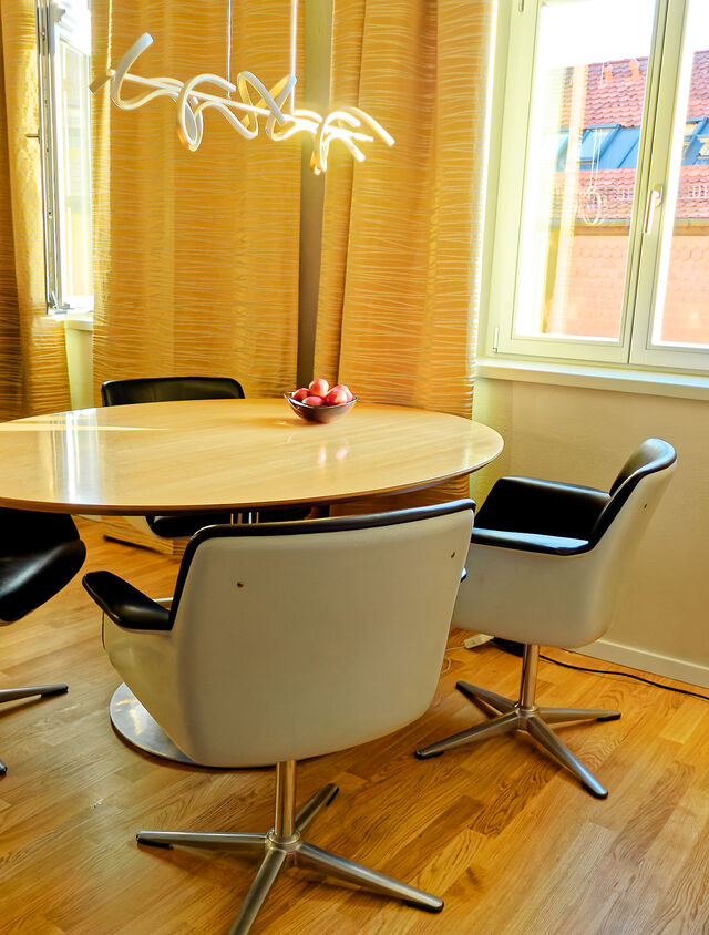 Heller Essbereich mit Pierre Paulin Designer-Tisch, Friso Kramer Drehst&uuml;hlen, goldenen Vorh&auml;ngen und Blick auf rote Ziegeld&auml;cher im m&ouml;blierten Premium-Apartment Bamberg Karmelitenkloster