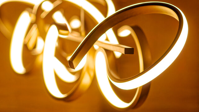 Nahaufnahme-Detail beleuchteter skulpturaler Pendelleuchte mit flie&szlig;enden gold-wei&szlig;en Metallringen f&uuml;r warmes Ambientelicht im m&ouml;blierten Apartment Bamberg