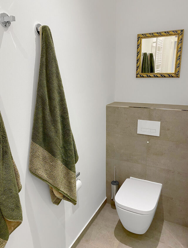 Modernes H&auml;nge-WC mit Premium-Handt&uuml;chern in Olivgr&uuml;n und ornamentalem Goldspiegel im m&ouml;blierten Apartment Bamberg and ornate gold mirror in furnished apartment Bamberg
