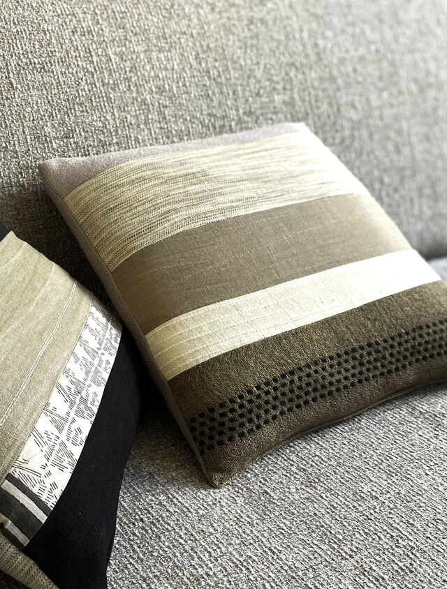 Nahaufnahme Designer-Sofa mit Dekokissen in gestreiften und strukturierten Mustern, nat&uuml;rliche Grau- und Beiget&ouml;ne mit verschiedenen Webstrukturen auf Salz-und-Pfeffer-Polster im m&ouml;blierten Apartment Bamberg