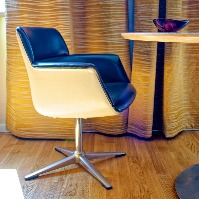 Friso Kramer Vintage-Designer-Drehstuhl mit schwarzem Kunstlederpolster und Chromgestell vor goldenen Vorh&auml;ngen im m&ouml;blierten Apartment Bamberg