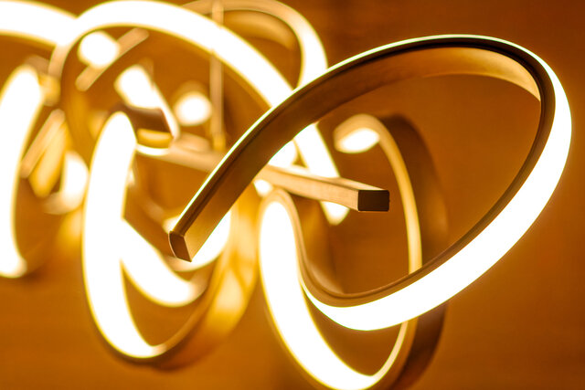 Nahaufnahme-Detail beleuchteter skulpturaler Pendelleuchte mit flie&szlig;enden gold-wei&szlig;en Metallringen f&uuml;r warmes Ambientelicht im m&ouml;blierten Apartment Bamberg
