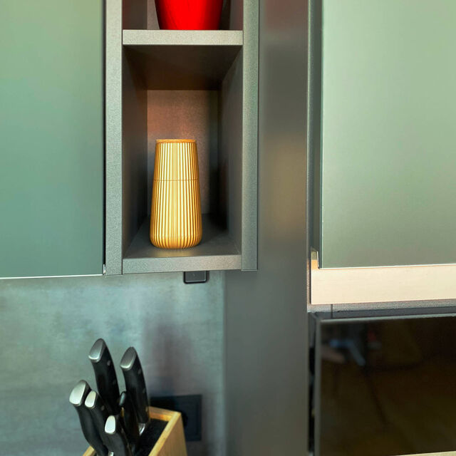 Nahaufnahme mineralgr&uuml;ne ultramatte Nobilia-K&uuml;che mit offenen Pr&auml;sentations-Nischen, roter Designer-Vase, hochwertigem Messerblock und Designer-Accessoires auf dunkler Arbeitsplatte im m&ouml;blierten Apartment Bamberg