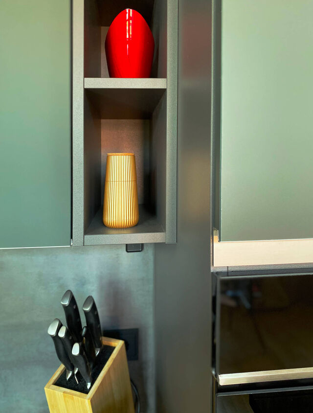 Nahaufnahme mineralgr&uuml;ne ultramatte Nobilia-K&uuml;che mit offenen Pr&auml;sentations-Nischen, roter Designer-Vase, hochwertigem Messerblock und Designer-Accessoires auf dunkler Arbeitsplatte im m&ouml;blierten Apartment Bamberg