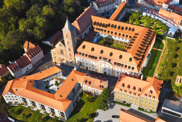 Luftaufnahme des renovierten Karmeliterklosters mit Kirche, rotem Ziegeldach, Dachgauben und Kopfsteinpflasterhof im historischen Bamberg
